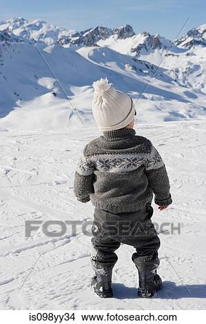 Young boy standing looking at mountains in snow View Large Photo Image Picture - Young boy standing looking at mountains in snow. Fotosearch