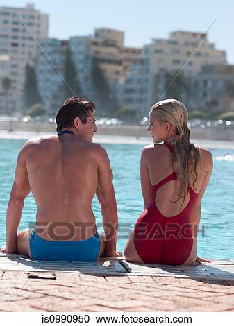 Stock Image - Young couple sitting at poolside. Fotosearch
