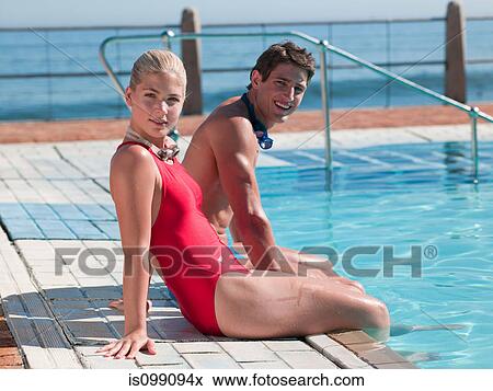 Stock Photo - Young couple sitting at poolside, portrait. Fotosearch