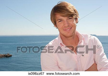 Young man in pink shirt by the ocean View Large Photo Image Stock Photo - Young man in pink shirt by the ocean. Fotosearch