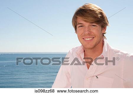Young man in pink shirt by the ocean View Large Photo Image Stock Photo - Young man in pink shirt by the ocean. Fotosearch