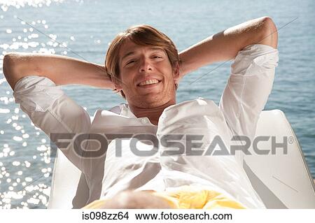Young man relaxing on lounger by the ocean View Large Photo Image Picture - Young man relaxing on lounger by the ocean. Fotosearch