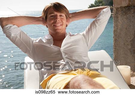 Young man relaxing on lounger by the ocean View Large Photo Image Stock Photography - Young man relaxing on lounger by the ocean. Fotosearch
