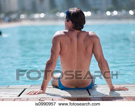 Stock Photo - Young man sitting at poolside. Fotosearch