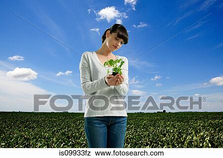 Stock Photo - Young woman holding plant in field. Fotosearch