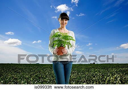 Stock Photograph - Young woman holding plant in field. Fotosearch