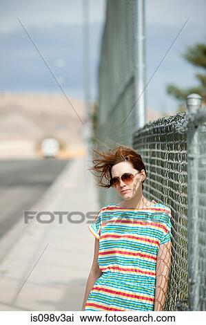 Stock Image - Young woman leaning on wire fence. Fotosearch