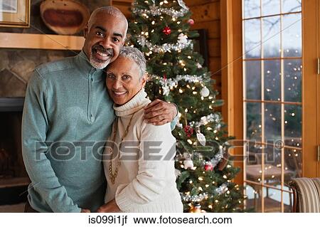 Stock Image - Mature couple embracing by Christmas tree, portrait. Fotosearch