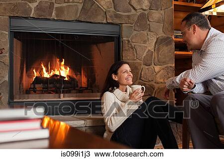 Stock Image - Mature couple relaxing by fireplace. Fotosearch