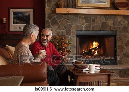 Stock Photograph - Mature couple sitting by fireplace. Fotosearch