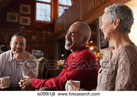 Stock Photo - Mature friends laughing together in living room. Fotosearch