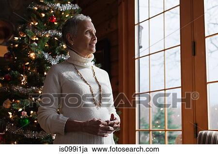 Mature woman standing by Christmas tree, looking through window View Large Photo Image Stock Image - Mature woman standing by Christmas tree, looking through window. Fotosearch