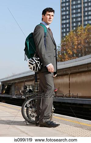 Stock Photo - Mid adult businessman carrying folding bicycle on railway platform. Fotosearch