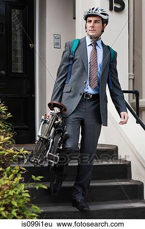 Stock Photograph - Mid adult businessman carrying folding bicycle down steps. Fotosearch