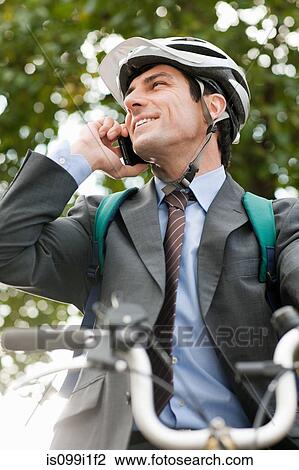 Stock Image - Mid adult businessman using cellphone on bicycle. Fotosearch
