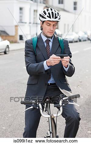 Stock Photo - Mid adult businessman using cellphone to text on bicycle. Fotosearch