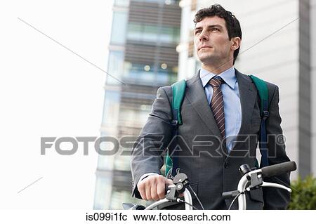 Stock Image - Mid adult businessman with bike in city. Fotosearch