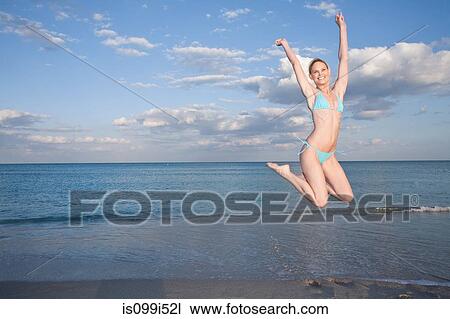 Mid adult woman in bikini leaping on beach View Large Photo Image Stock Image - Mid adult woman in bikini leaping on beach. Fotosearch