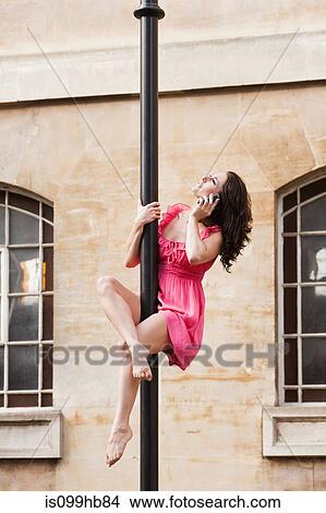Picture - Mid adult woman in pink dress using cellphone on street lamp in city. Fotosearch