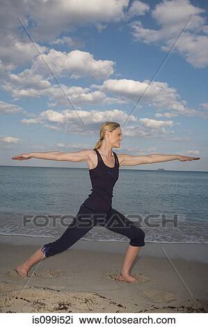 Stock Image - Mid adult woman in yoga pose on beach. Fotosearch