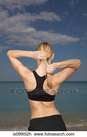 Stock Image - Mid adult woman tying ponytail, rear view. Fotosearch