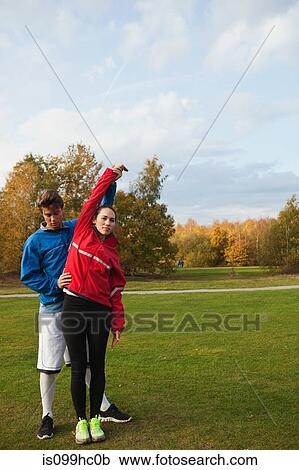 Stock Image - Personal trainer assisting young woman with warm up exercises. Fotosearch