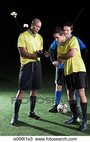 Stock Image - Soccer players looking at cellphone on pitch. Fotosearch