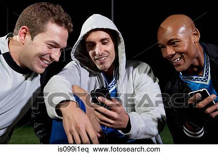 Stock Photography - Soccer players looking at cellphone on pitch. Fotosearch