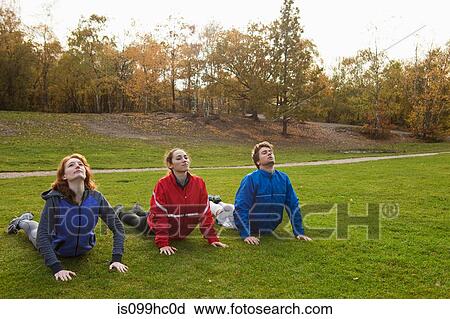 Stock Image - Three young friends stretching on grass in park. Fotosearch