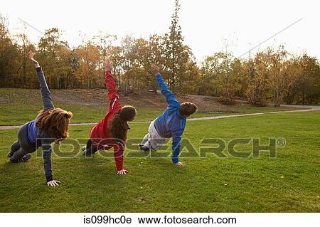 Three young friends stretching on grass in park View Large Photo Image Stock Image - Three young friends stretching on grass in park. Fotosearch