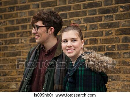 Stock Photography - Young couple by brick wall, smiling. Fotosearch