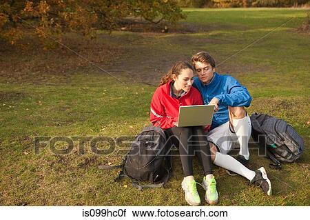 Stock Image - Young couple using laptop in park. Fotosearch