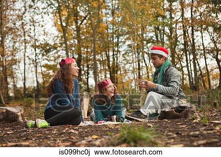 Stock Image - Young friends in forest wearing Santa hats and crowns. Fotosearch