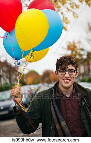 Stock Photo - Young man holding colourful balloons, portrait. Fotosearch