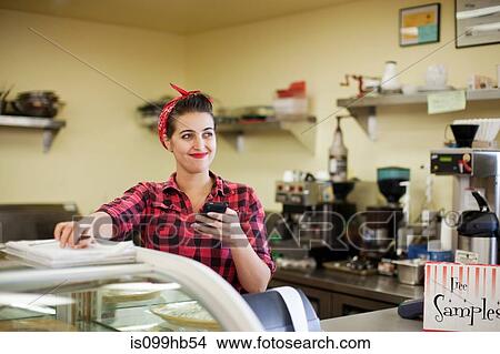 Picture - Young woman holding cellphone in bakery. Fotosearch