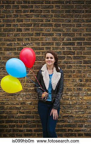 Young woman holding colourful balloons against brick wall View Large Photo Image Picture - Young woman holding colourful balloons against brick wall. Fotosearch