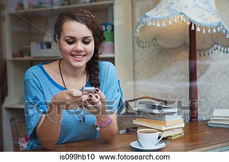 Stock Image - Young woman in cafe using cell phone. Fotosearch