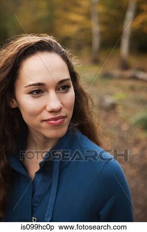 Stock Photography - Young woman in forest smiling, looking away. Fotosearch