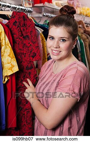 Young woman looking at dress in clothes shop, portrait View Large Photo Image Stock Photo - Young woman looking at dress in clothes shop, portrait. Fotosearch