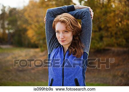 Stock Photograph - Young woman performing stretches in park. Fotosearch