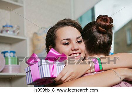Young women holding birthday gift and embracing View Large Photo Image Stock Photo - Young women holding birthday gift and embracing. Fotosearch