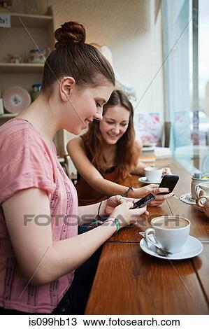 Young women in cafe using cell phones View Large Photo Image Stock Image - Young women in cafe using cell phones. Fotosearch