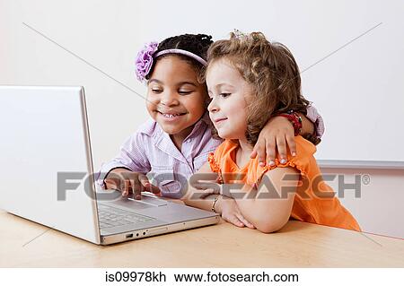 Stock Image - Girls looking at laptop together. Fotosearch