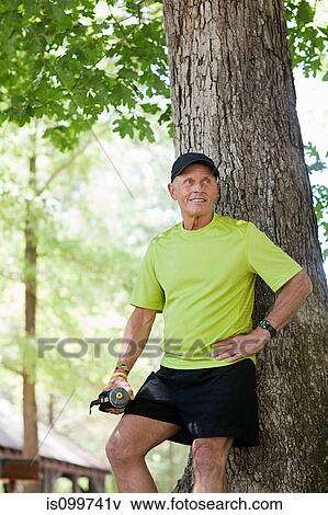 Man leaning against tree holding water bottle View Large Photo Image Stock Photo - Man leaning against tree holding water bottle. Fotosearch