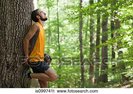 Man leaning against tree holding water bottle View Large Photo Image Stock Photograph - Man leaning against tree holding water bottle. Fotosearch
