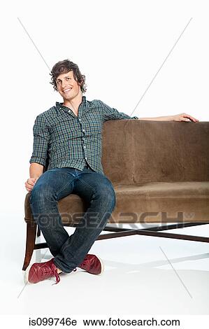 Stock Image - Mid adult man on sofa against white background. Fotosearch