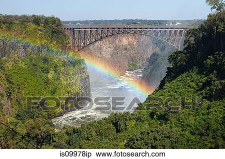 Rainbow over the Zambezi River and Victoria Falls Bridge. Zambia on right of bridge, Zimbabwe on left View Large Photo Image Stock Photography - Rainbow over the Zambezi River and Victoria Falls Bridge. Zambia on right of bridge, Zimbabwe on left. Fotosearch
