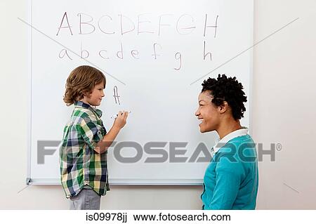 Stock Image - Teacher and boy writing alphabet on whiteboard. Fotosearch