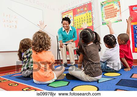 Picture of Teacher and children sitting on floors with hands raised ...