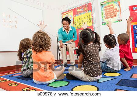 Teacher and children sitting on floors with hands raised View Large Photo Image Stock Photo - Teacher and children sitting on floors with hands raised. Fotosearch